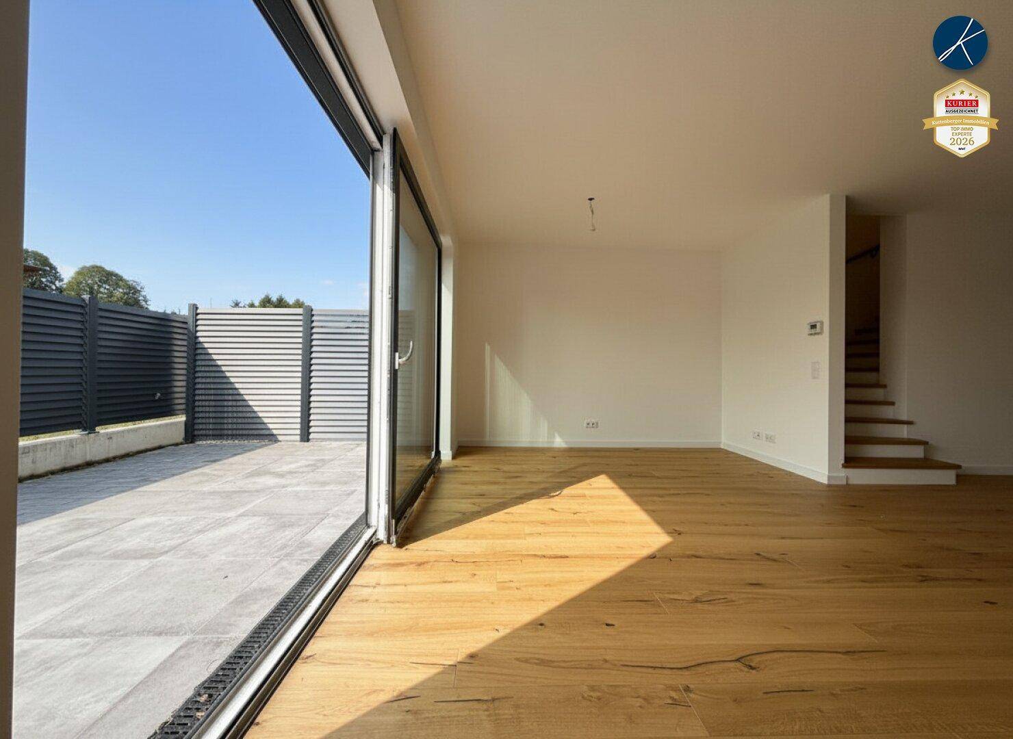 Geräumiges, leeres Wohnzimmer mit Holzboden und Zugang zu einer großen Außenterrasse.
