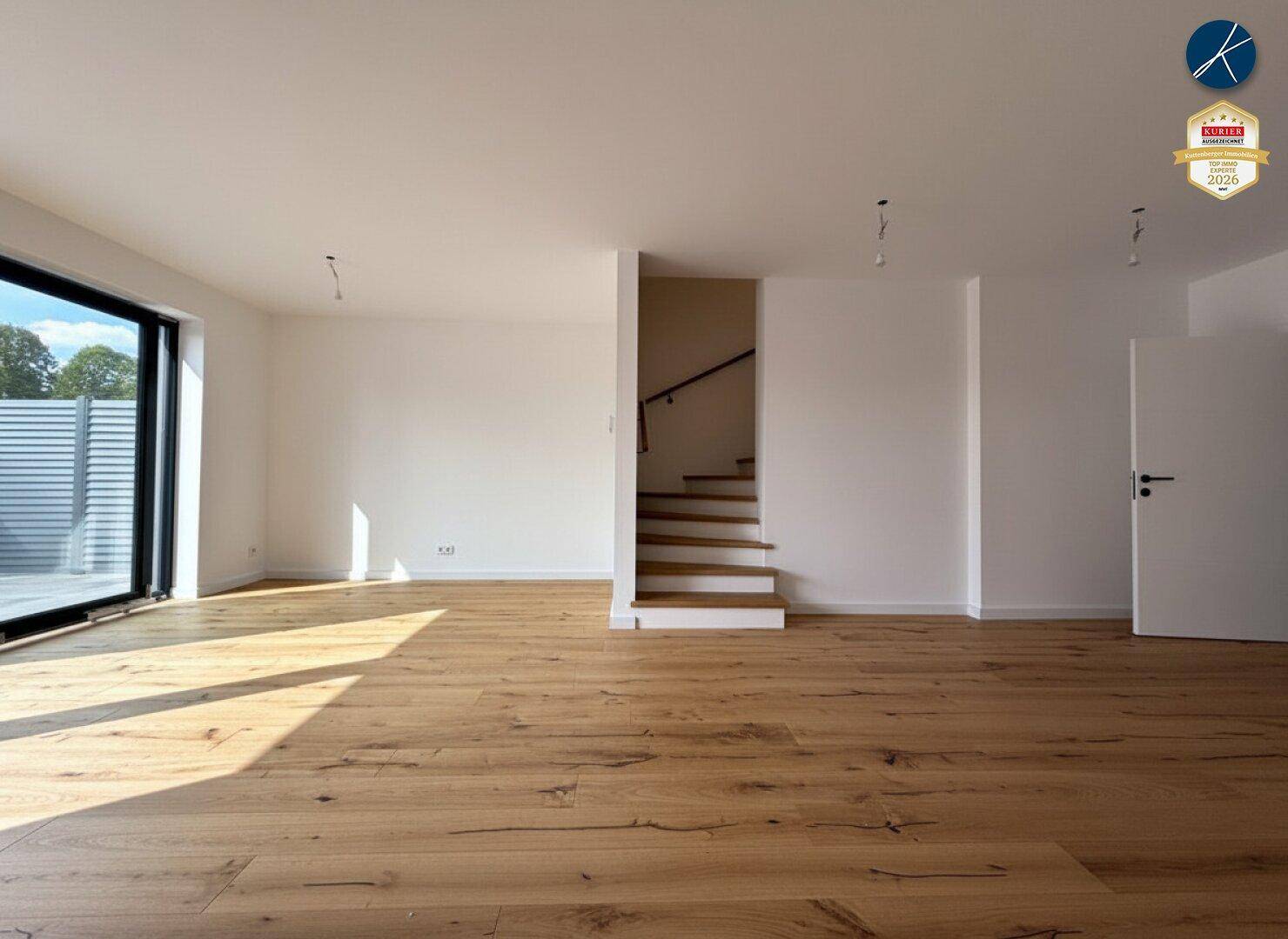 Geräumiger, leerer Raum mit Holzboden und einer Holztreppe, die in die obere Etage führt.