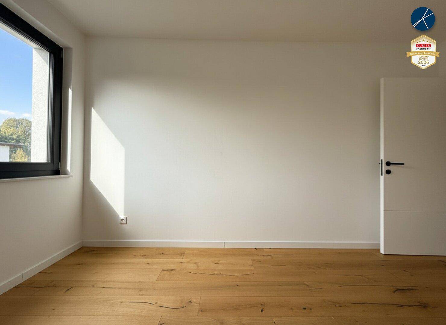 Heller, leerer Raum mit Holzboden und einem Fenster, das viel Tageslicht hereinlässt.