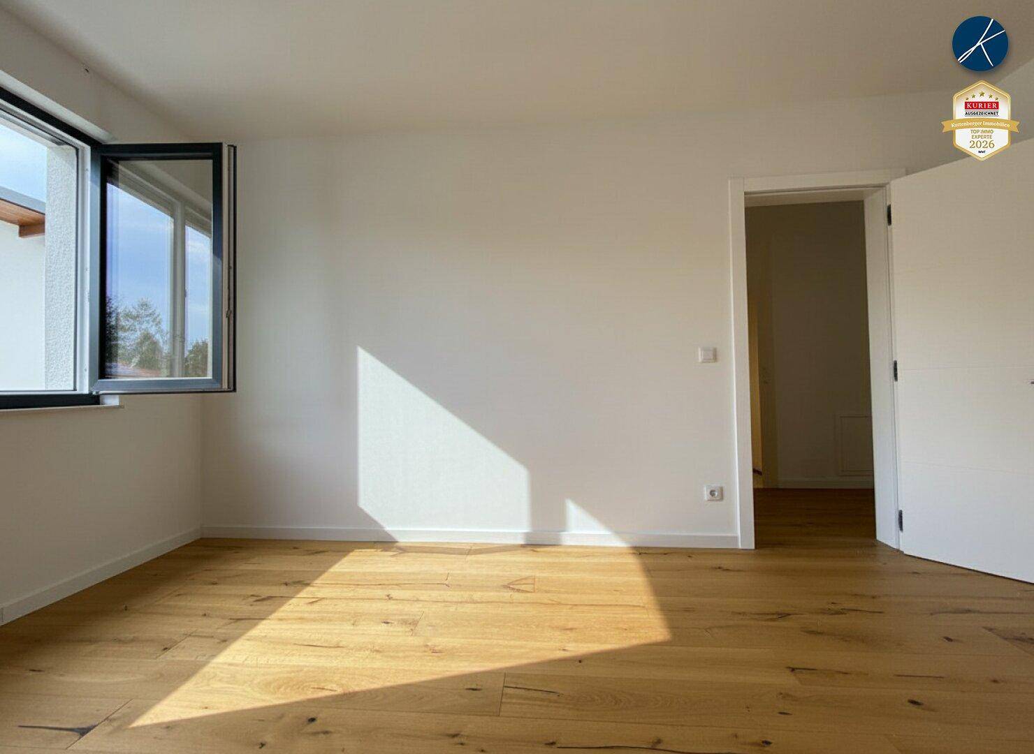 Helles, leeres Zimmer mit Eichenparkettboden und großen Fenstern, das viel Sonnenlicht hereinlässt.