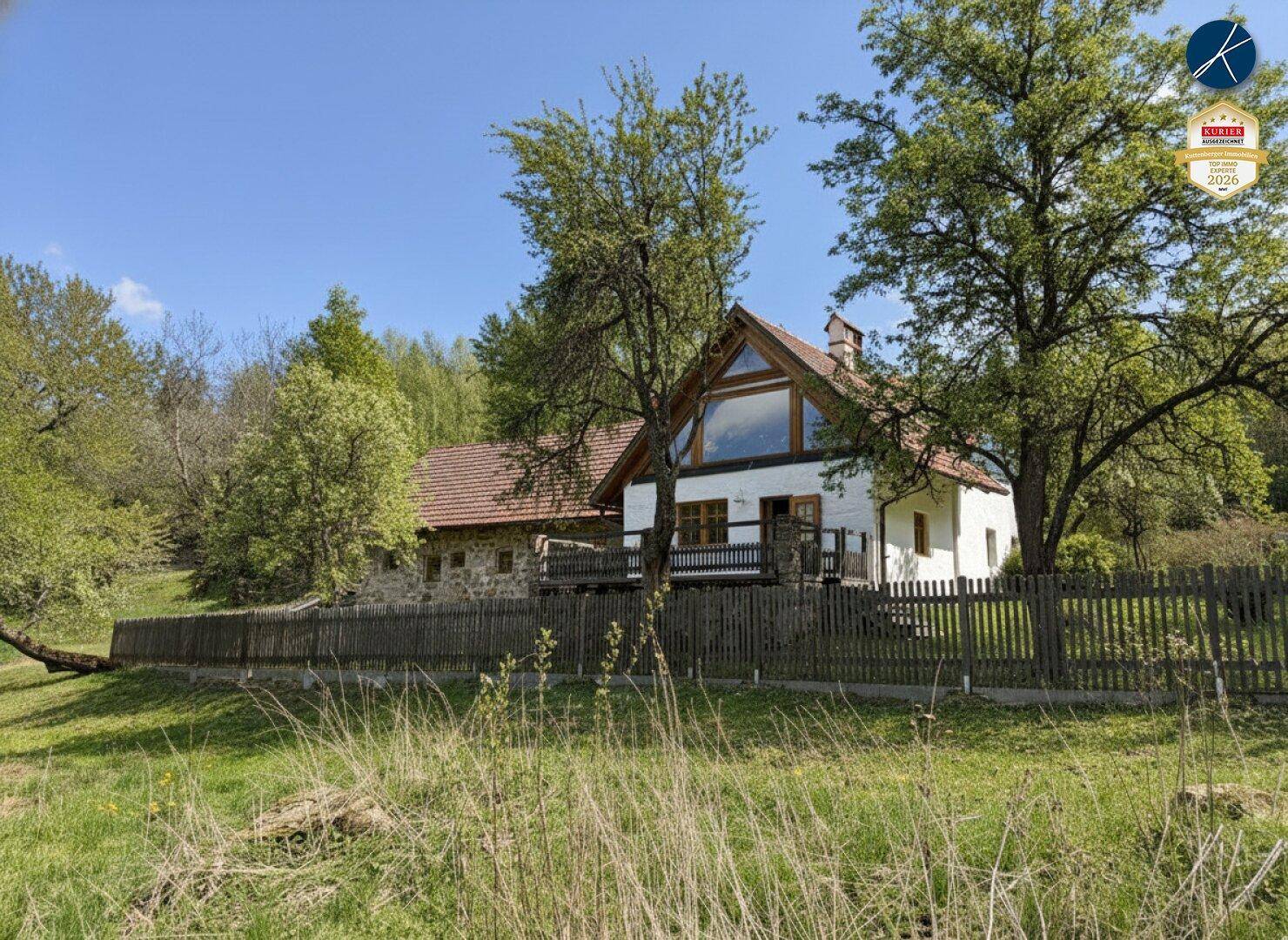 Charmantes Landhaus mit großer Fensterfront im Giebel und Holzbalkon in ländlicher Umgebung.