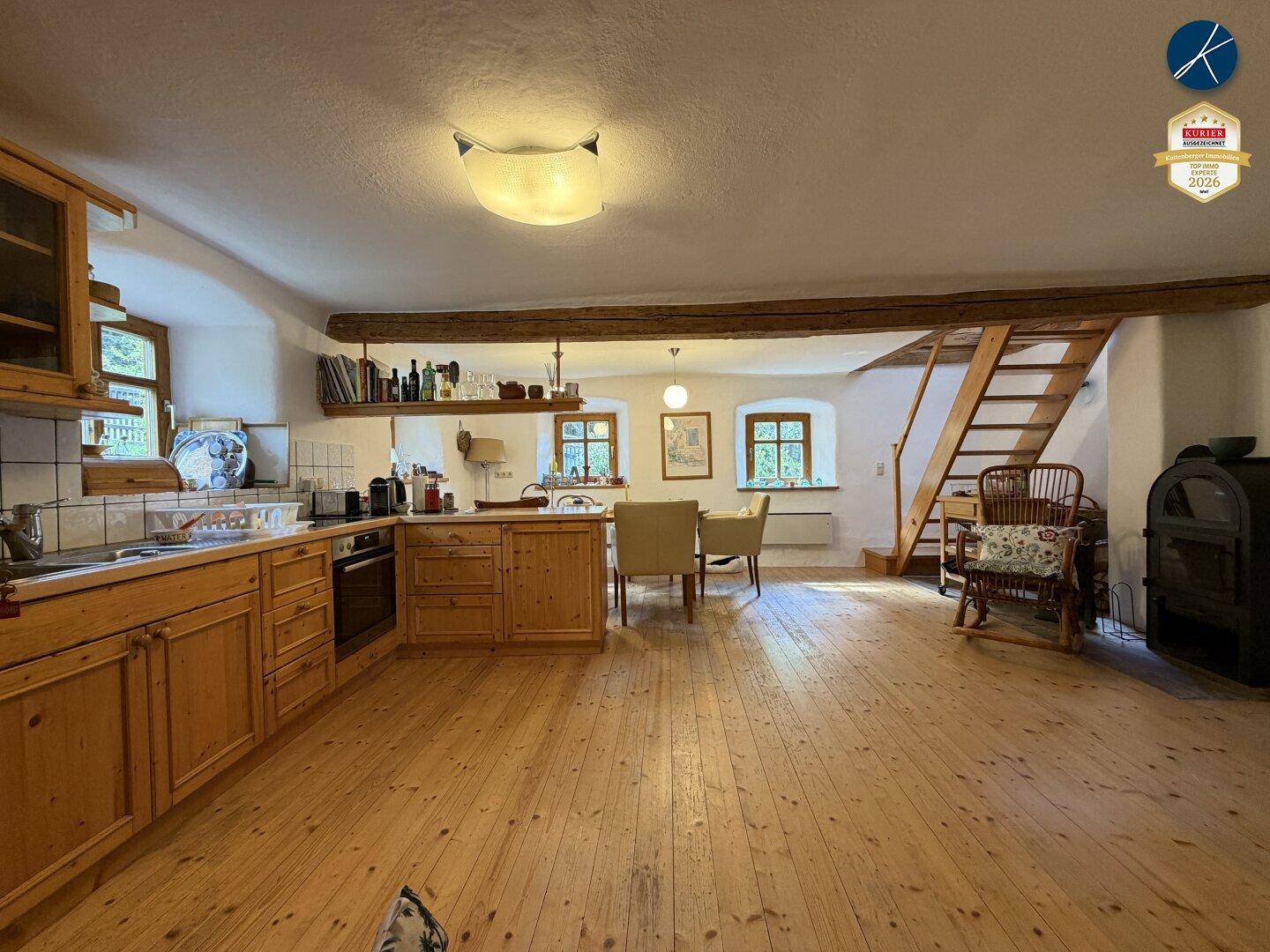 Gemütliche Wohnküche mit Holzboden, Holzmöbeln und einem Kaminofen, offen gestaltet.