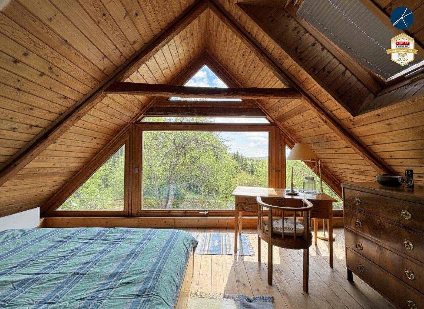 Schlafzimmer im Dachgeschoss mit Holztäfelung, großen Giebelfenstern und Blick ins Grüne.
