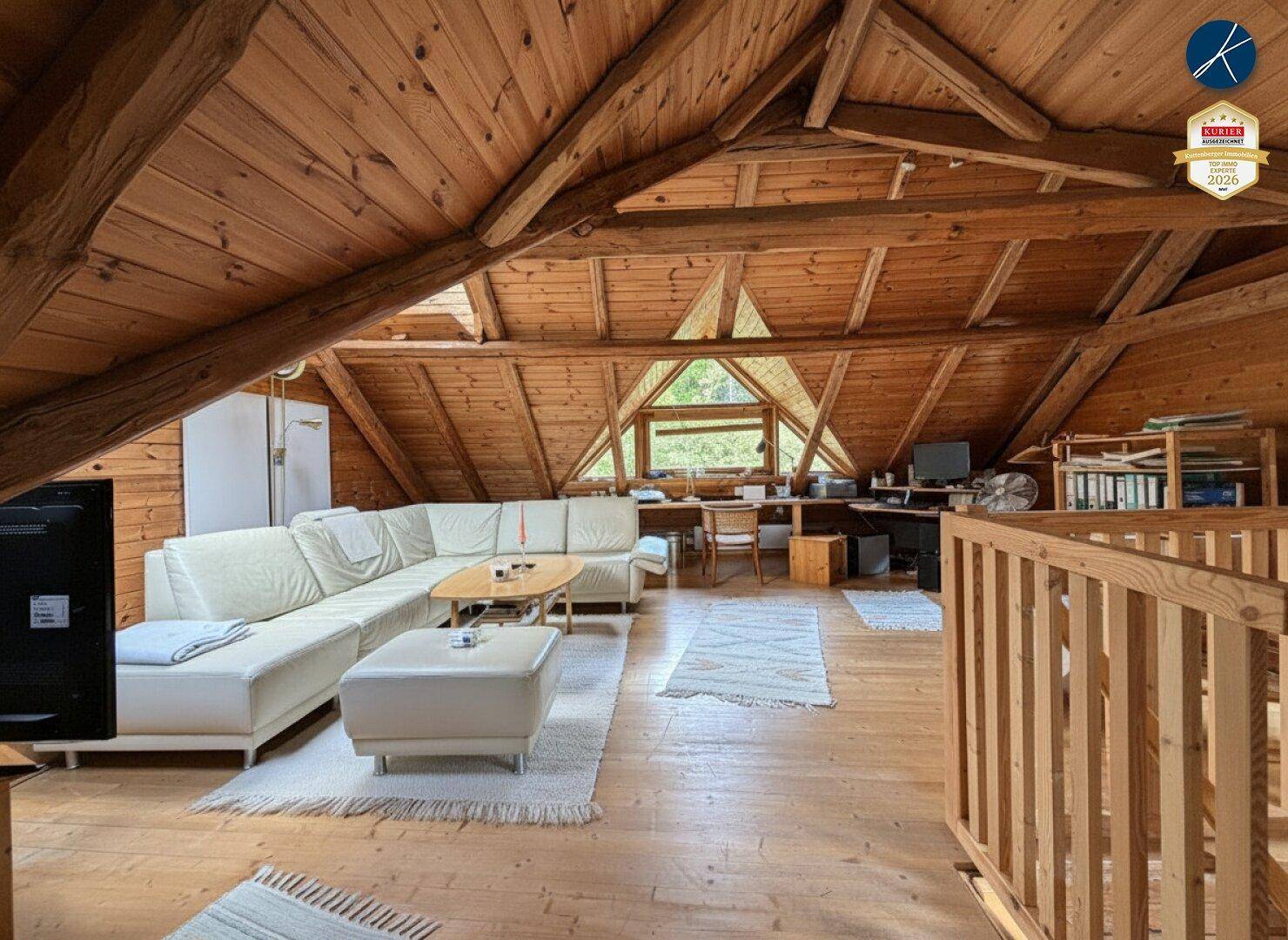 Geräumiger Wohnbereich im Dachgeschoss mit Holzbalken, gemütlicher Sitzecke und Arbeitsbereich.