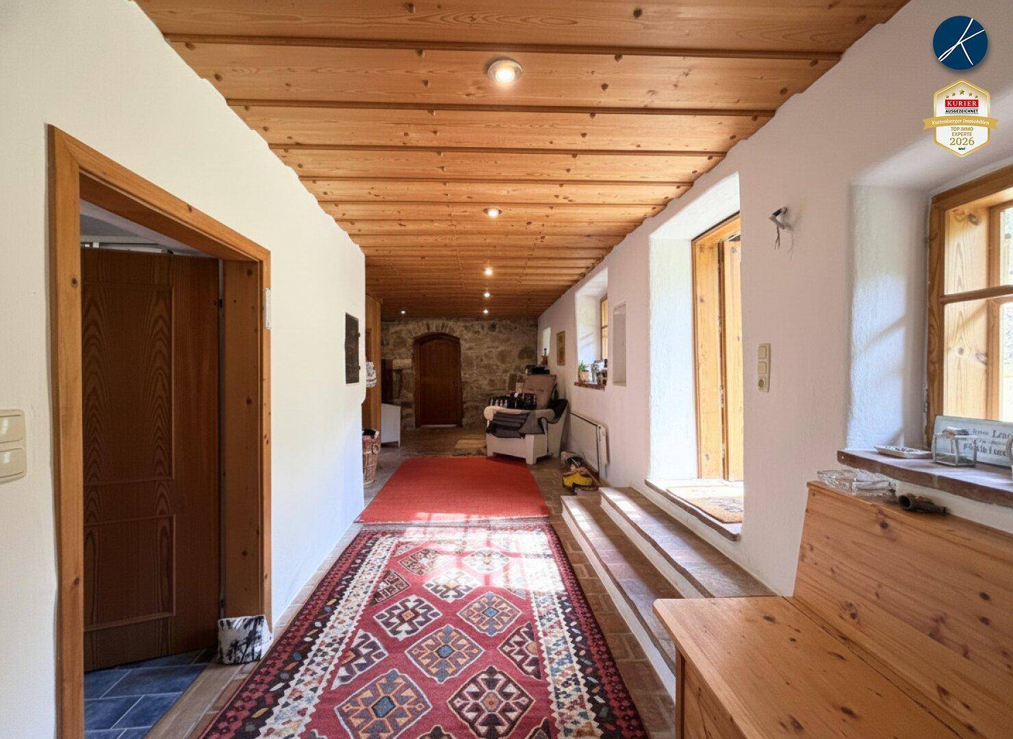 Rustikaler Flur mit Holzbalkendecke, Terrakottaboden und einem langen roten Teppich.