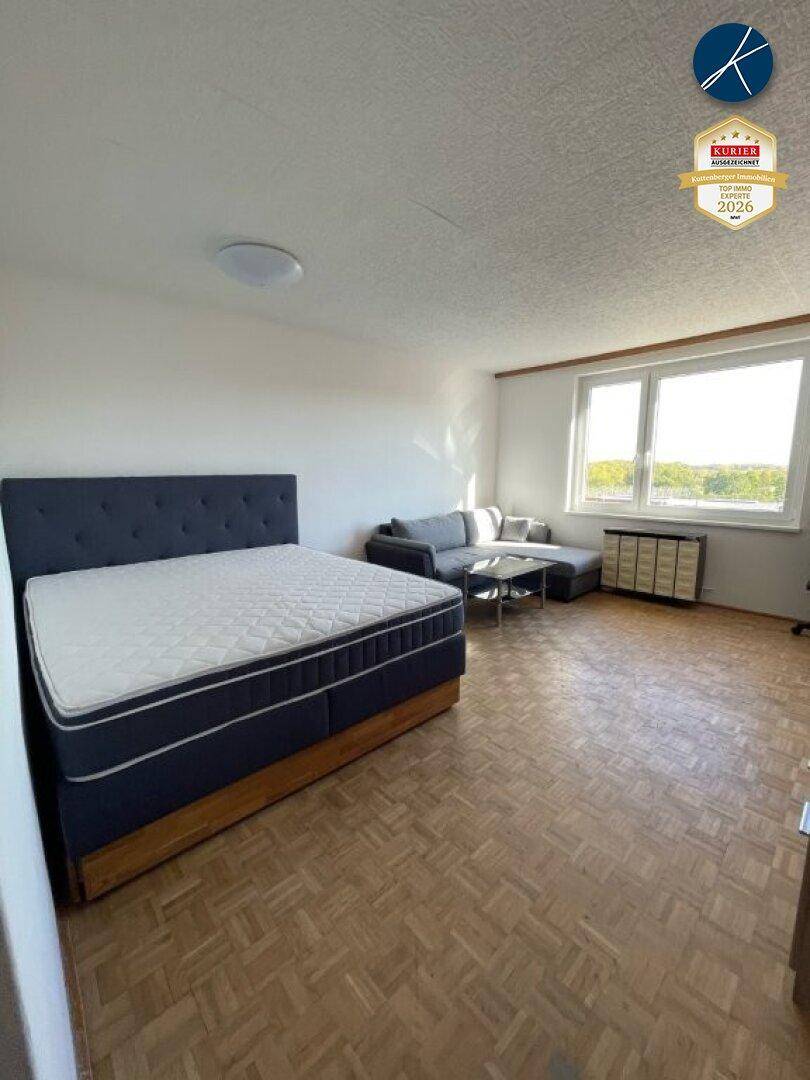 Geräumiges Schlafzimmer mit großem Bett und einer Sitzecke im Hintergrund, ausgestattet mit Parkettboden.
