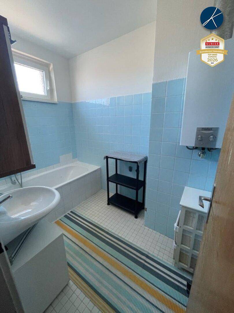Badezimmer mit hellblauen Fliesen, einer Badewanne und einem Waschbecken, beleuchtet durch ein Fenster.