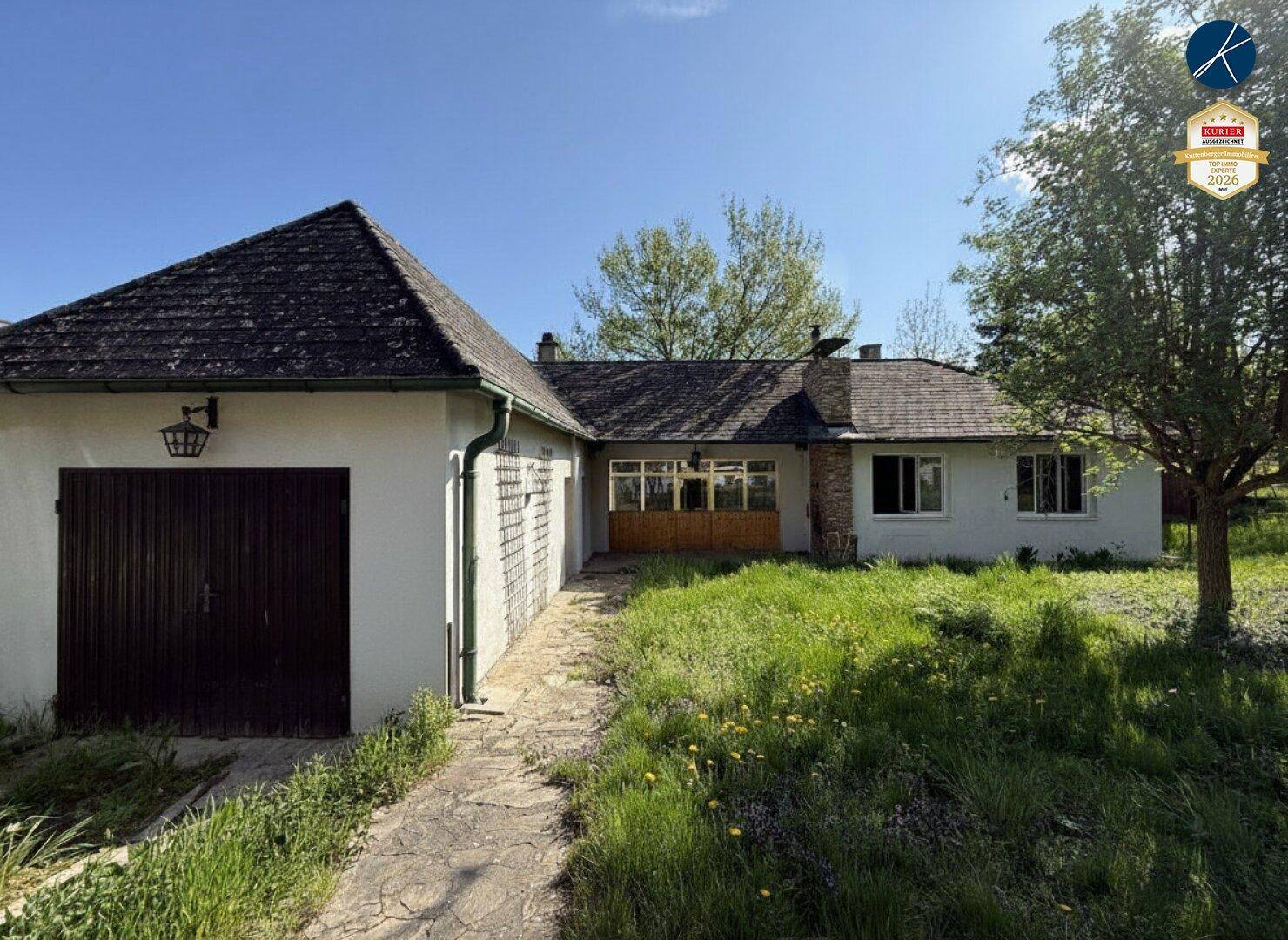 Ansicht des Hauses mit Garage und Gartenbereich unter blauem Himmel.