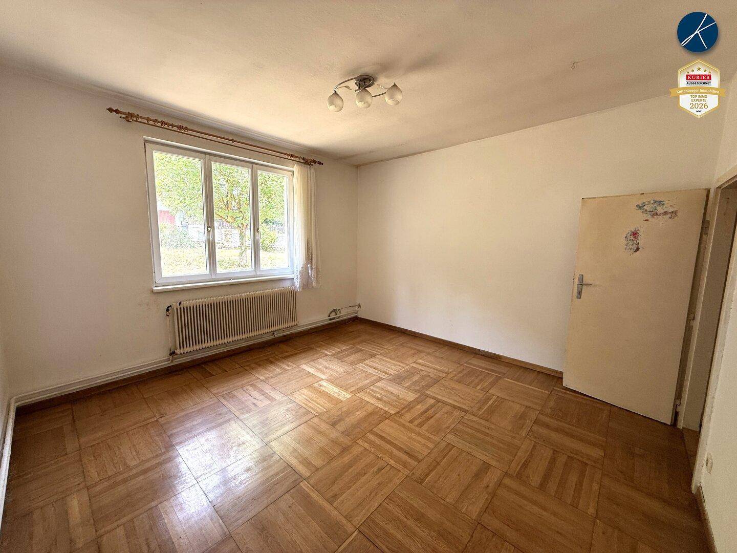 Geräumiges Schlafzimmer mit Parkettboden, Fenster und einfacher Deckenleuchte.