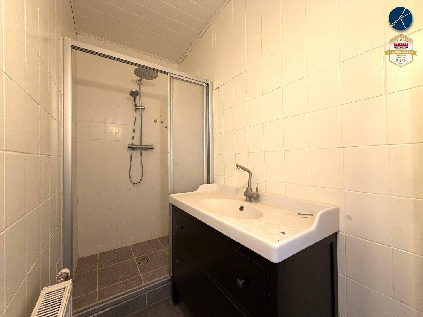 Kleines Badezimmer mit Duschkabine, Waschbecken und hellen Fliesen.