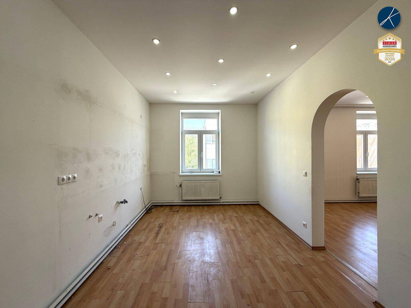 Leerer Raum, vorbereitet für eine Küche, mit Parkettboden und einem Fenster.