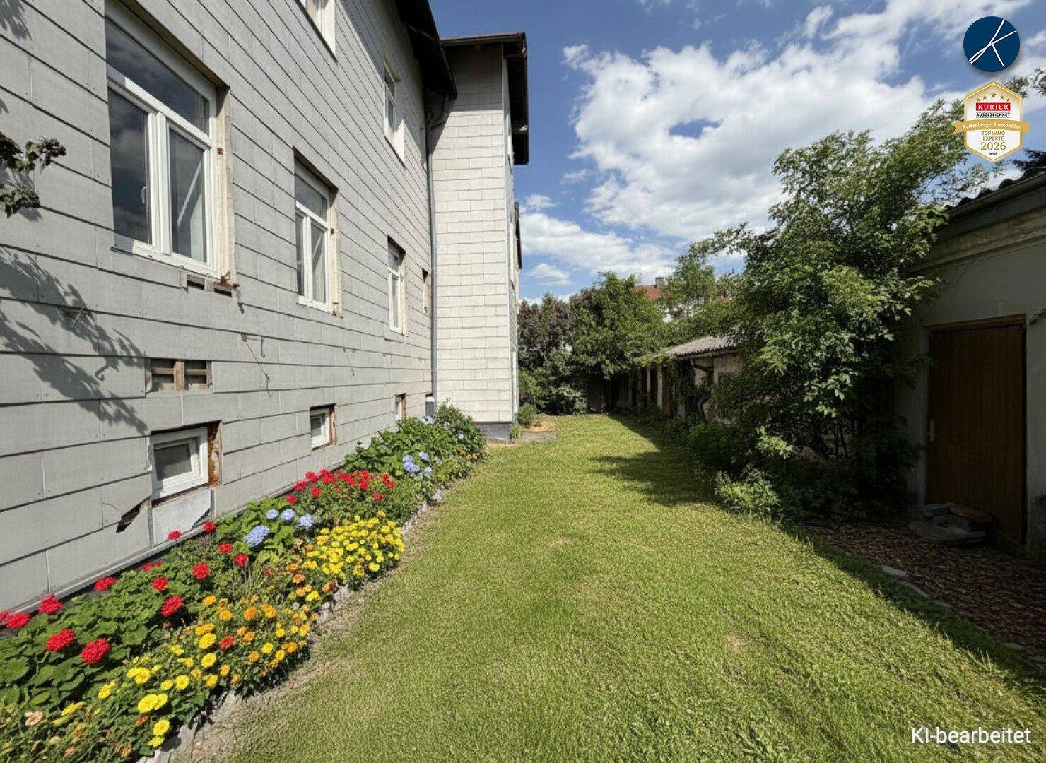 Gepflegter Gartenbereich mit Rasenfläche, bunten Blumenbeeten und seitlichem Blick auf das Gebäude.