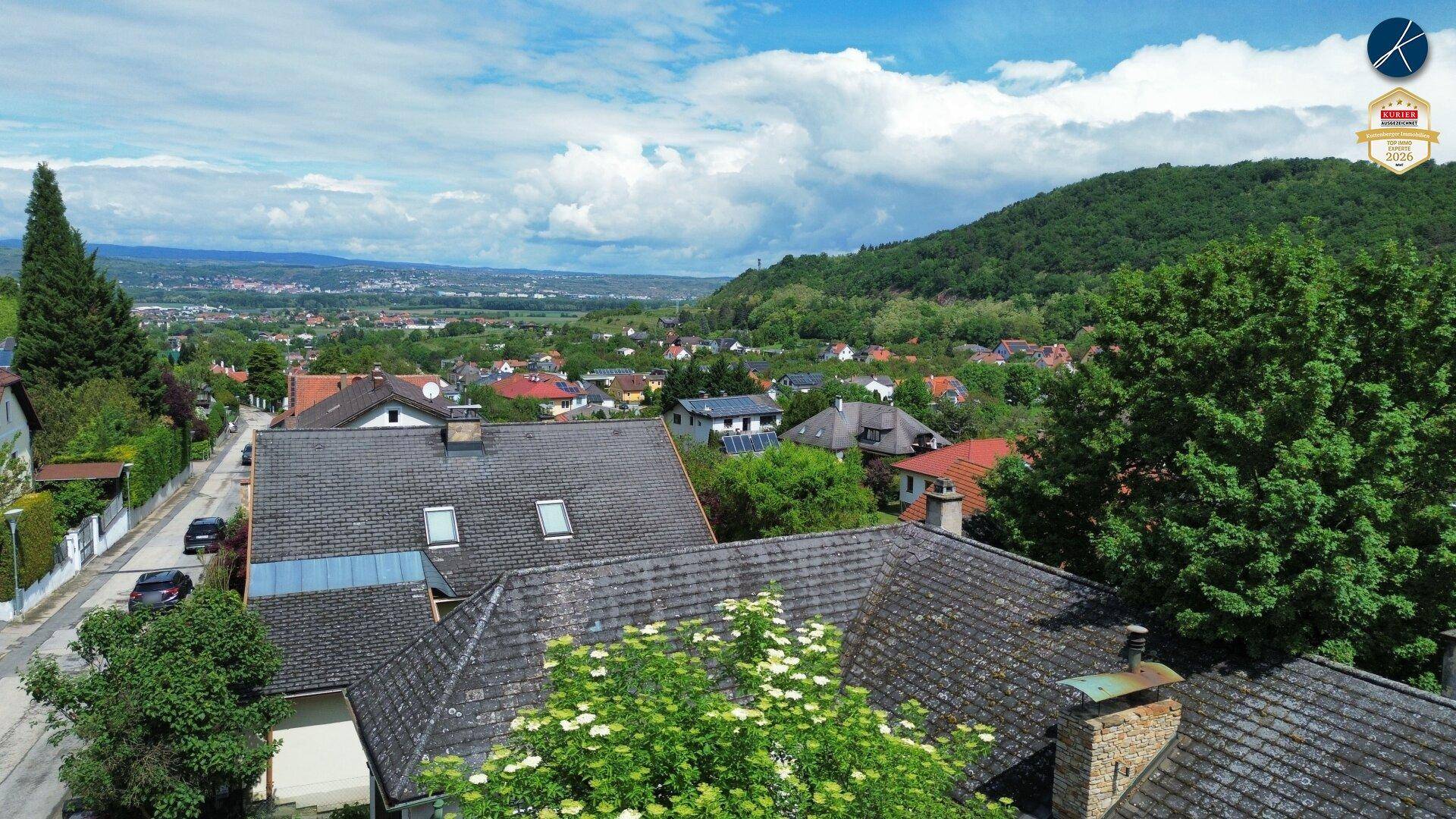 Weitblick über Dächer und grüne Hügel in eine ländliche Landschaft unter bewölktem Himmel.