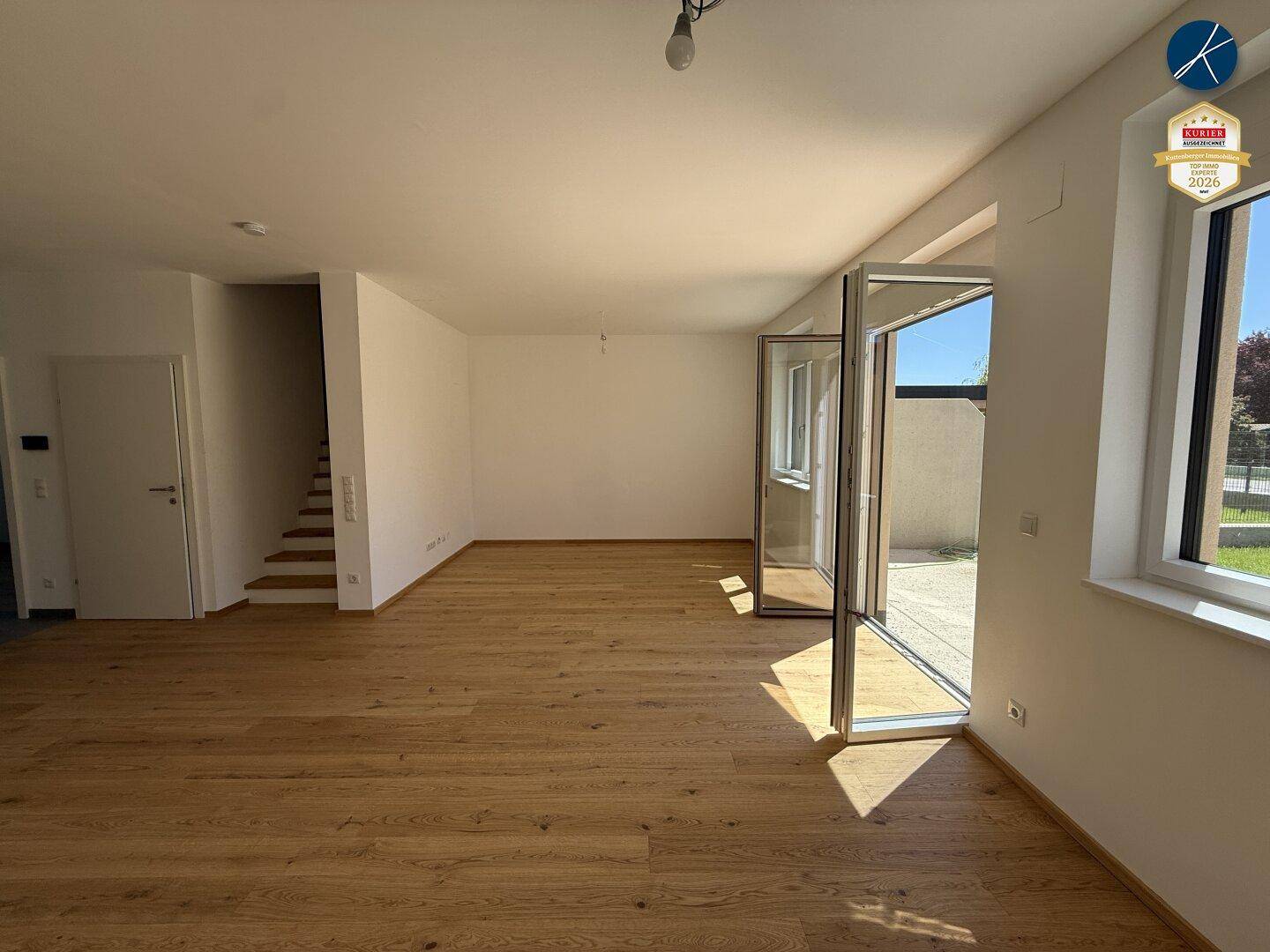 Geräumiges, leeres Wohnzimmer mit Holzboden und Zugang zur Terrasse, lichtdurchflutet.