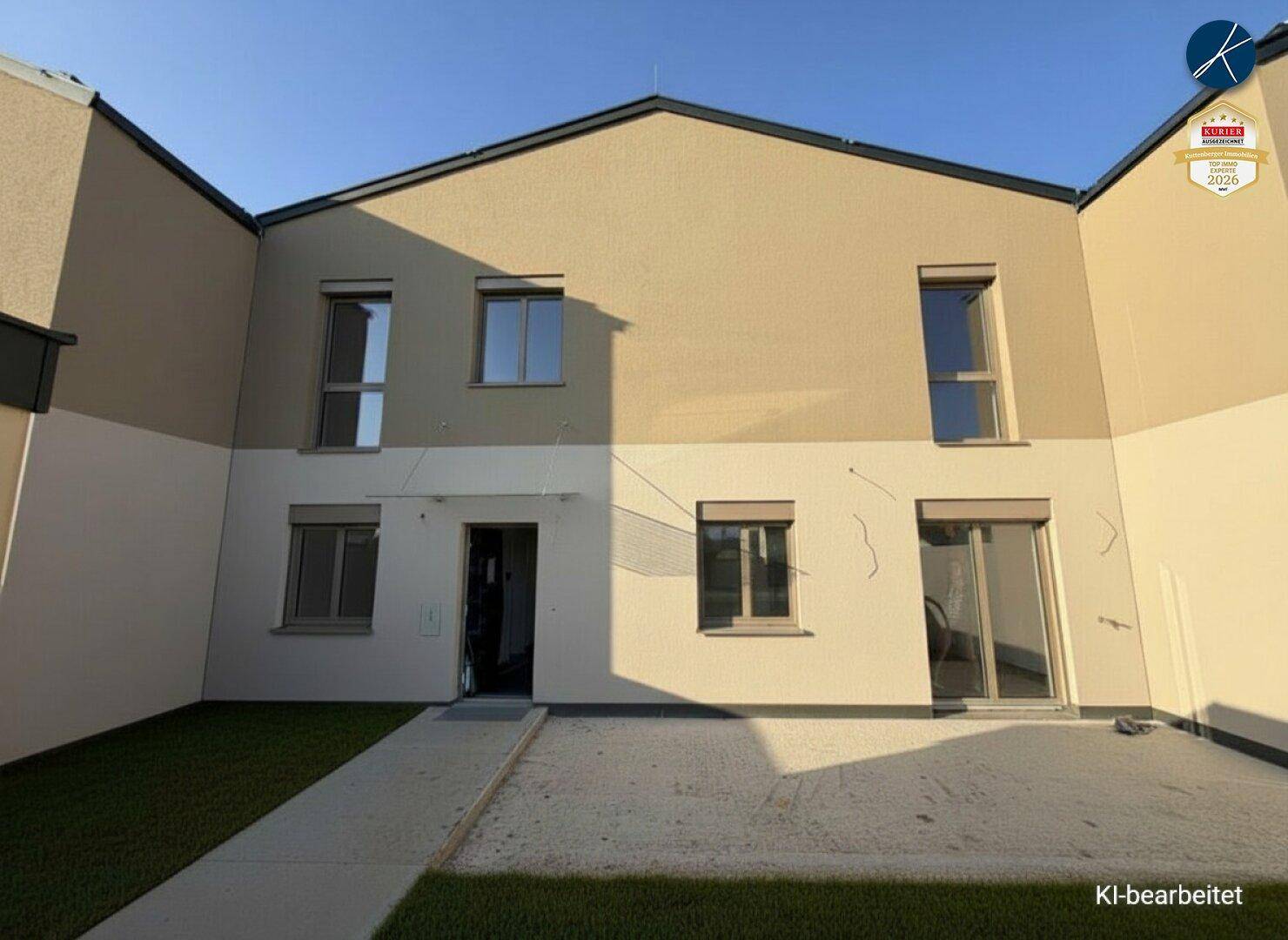 Unmöblierte Terrasse mit angrenzendem Gartenbereich und Blick auf die moderne Hausfassade.