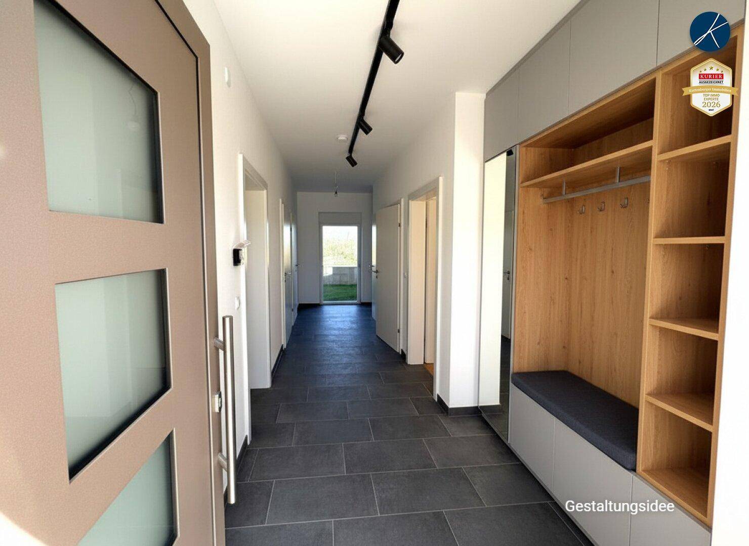 Heller Flur mit dunklen Fliesen, moderner Garderobe und Blick ins Grüne.