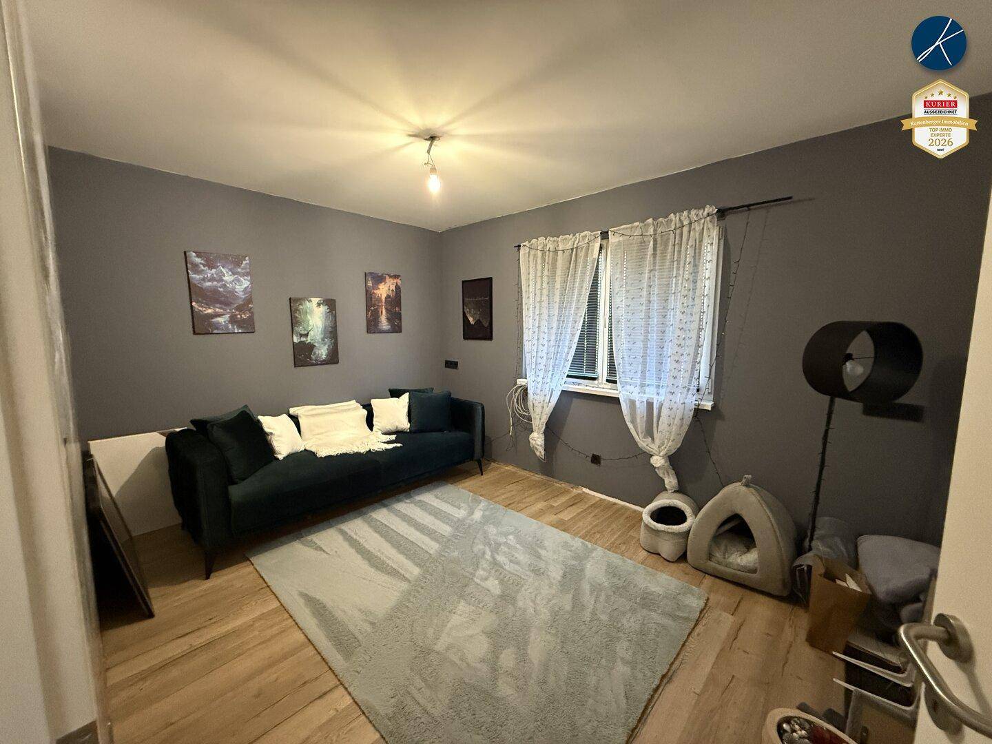 Gemütliches Wohnzimmer mit dunklem Sofa, hellem Teppich und Holzboden, dekoriert mit Bildern.