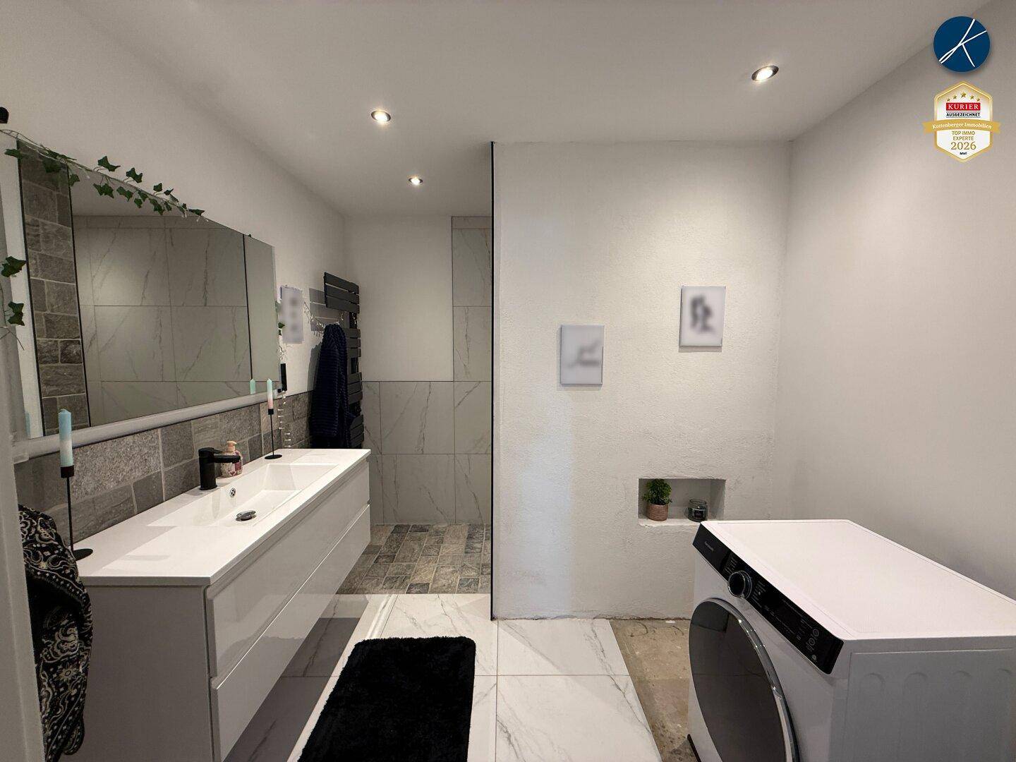 Modernes Badezimmer mit Doppelwaschbecken, großer Spiegelfläche und integrierter Waschmaschine.