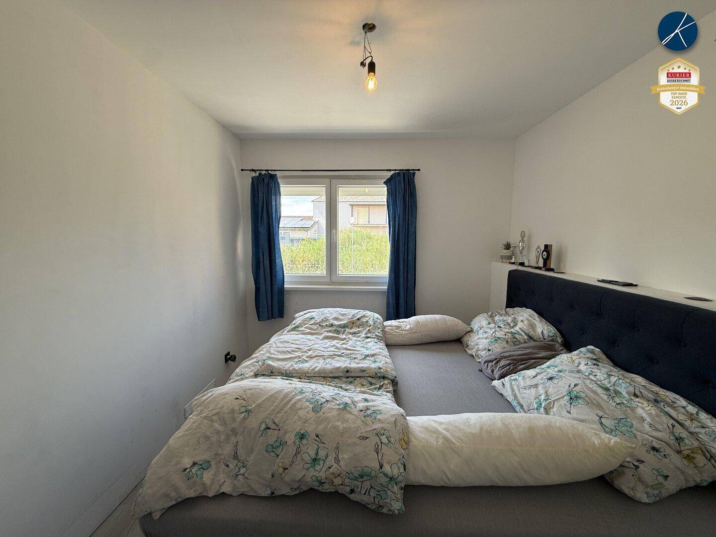 Helles Schlafzimmer mit Doppelbett, blauen Vorhängen und einem Fenster für natürliche Belichtung.
