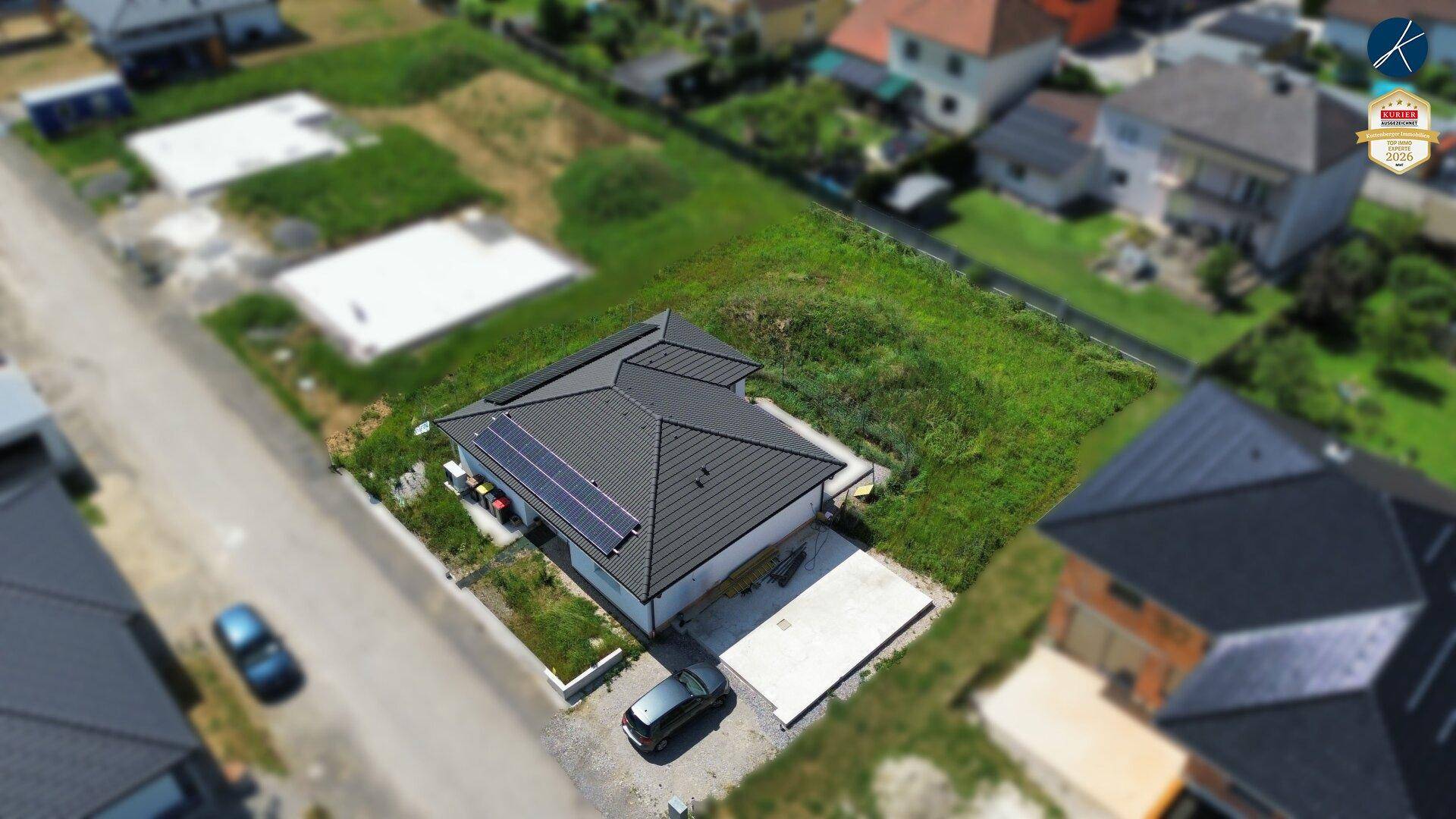 Vogelperspektive eines Einfamilienhauses mit Solarmodulen und angrenzenden unbebauten Grundstücken.