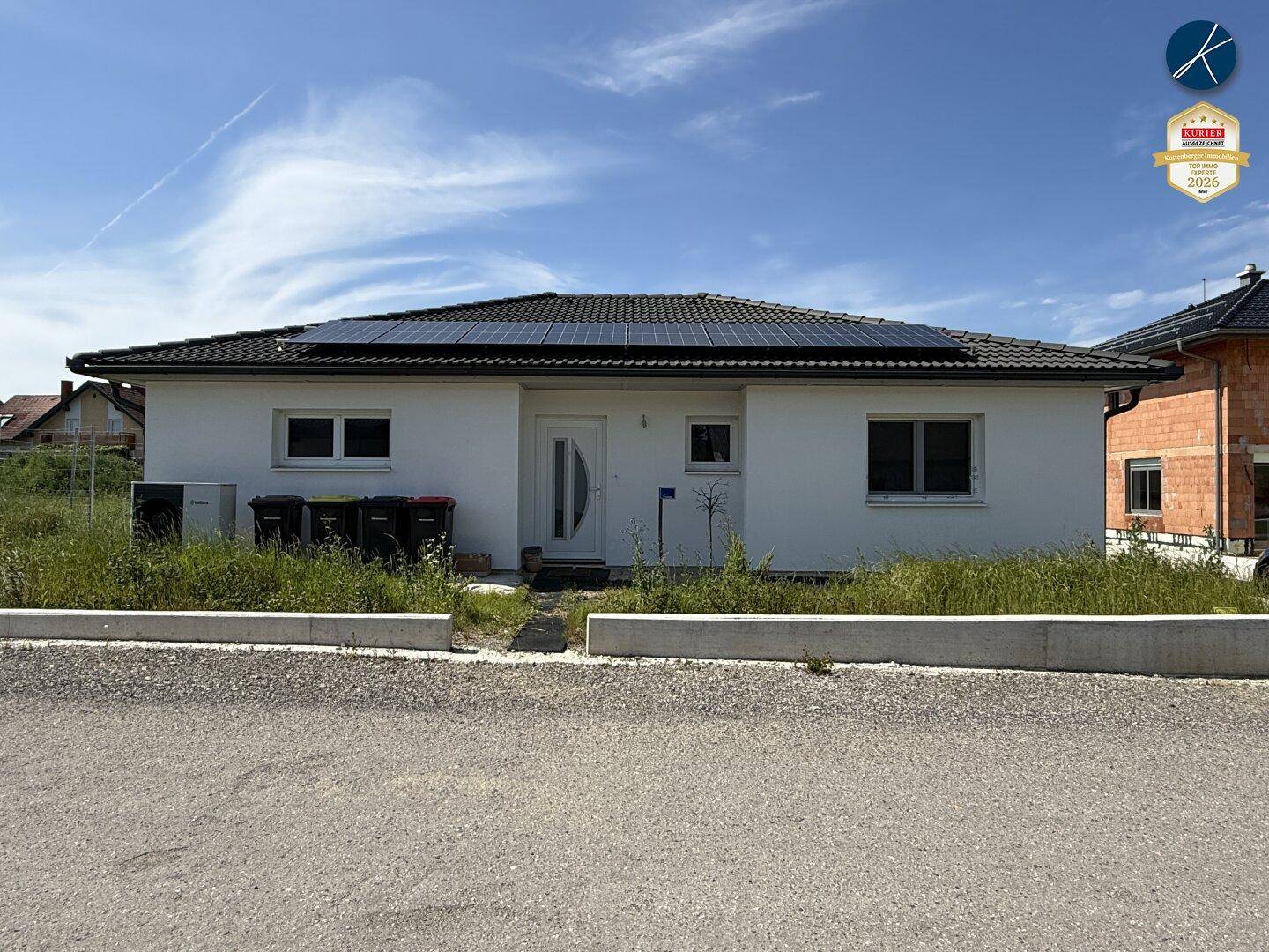 Frontansicht eines modernen Einfamilienhauses mit weißer Fassade und Solaranlage auf dem Dach.