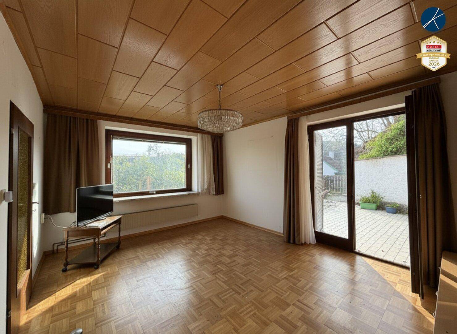 Geräumiges Wohnzimmer mit Parkettboden, Holzdecke und Zugang zu einer Außenterrasse.