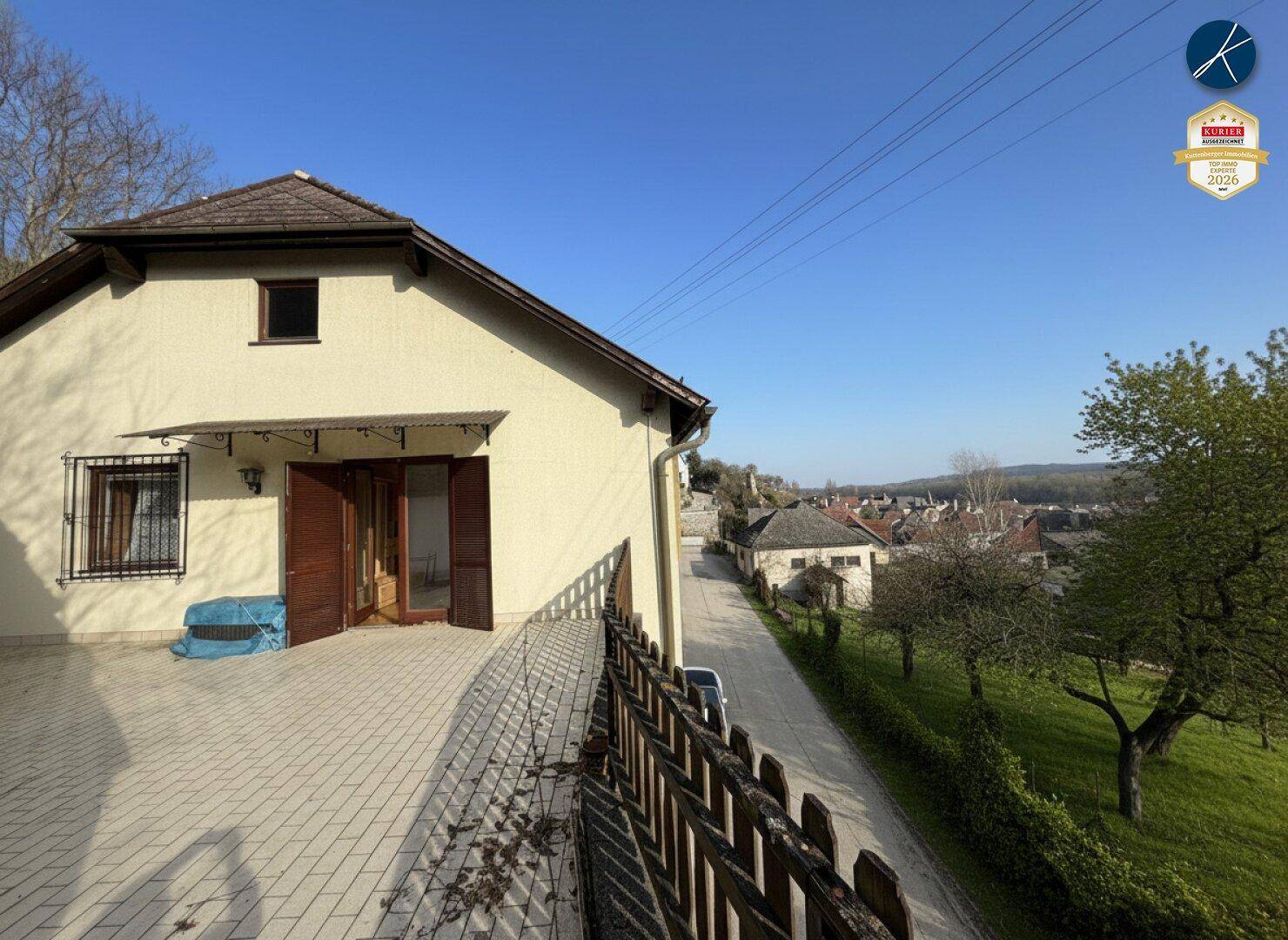 Große gepflasterte Terrasse am Haus mit Holzzaun und weitem Blick auf die Umgebung.