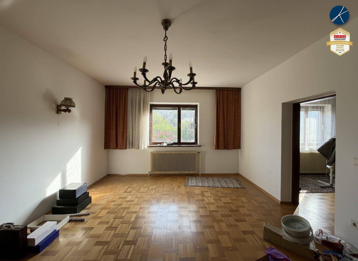 Helles Wohnzimmer mit Parkettboden, großem Fenster und traditionellem Kronleuchter, bereit zur Gestaltung.