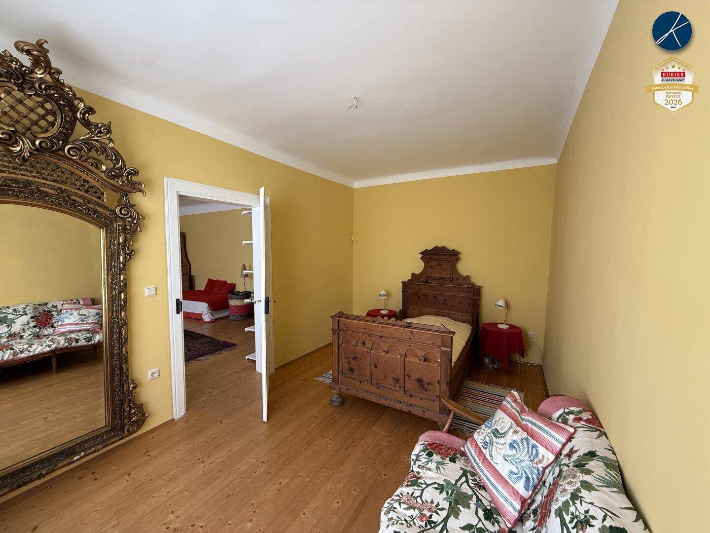 Schlafzimmer mit Holzboden, gelben Wänden und einem großen, verzierten Spiegel, traditionell eingerichtet.