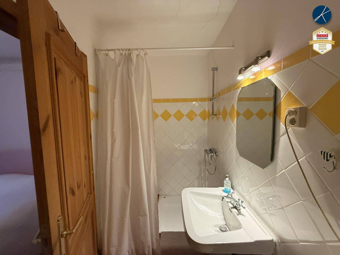 Badezimmer mit gelb-weißen Fliesen, Dusche und Waschbecken, traditionell eingerichtet.