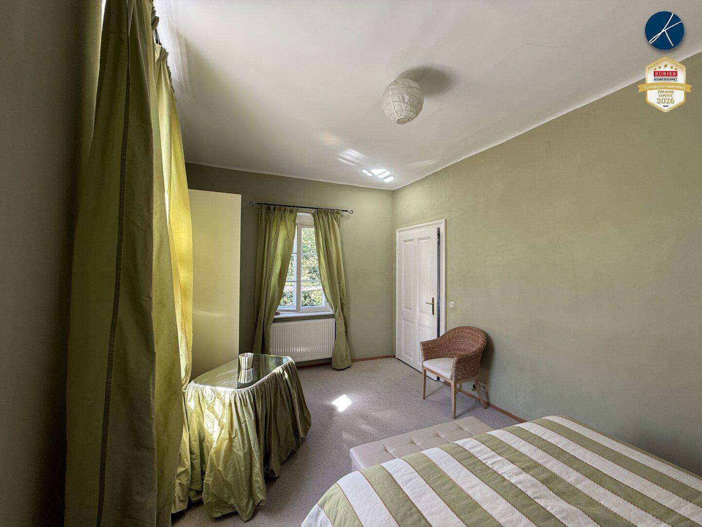 Helles Schlafzimmer mit Teppichboden und grünen Wänden, ausgestattet mit einem Fenster und Vorhängen.