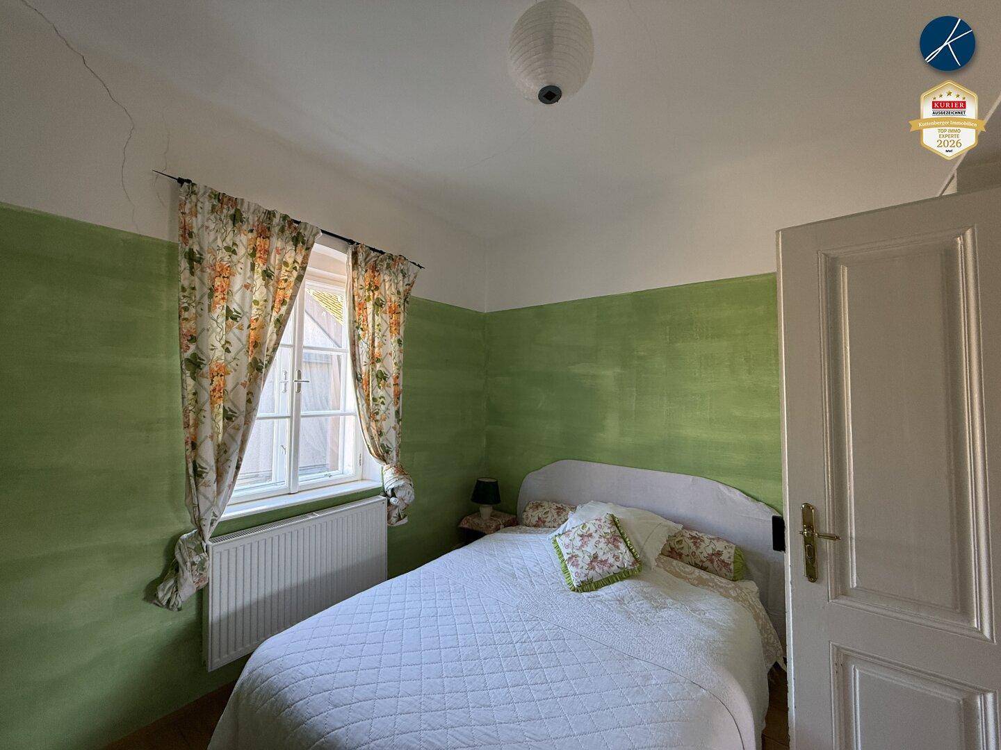 Schlafzimmer mit grün gestrichenen Wänden und einem Fenster, das natürliches Licht hereinlässt.