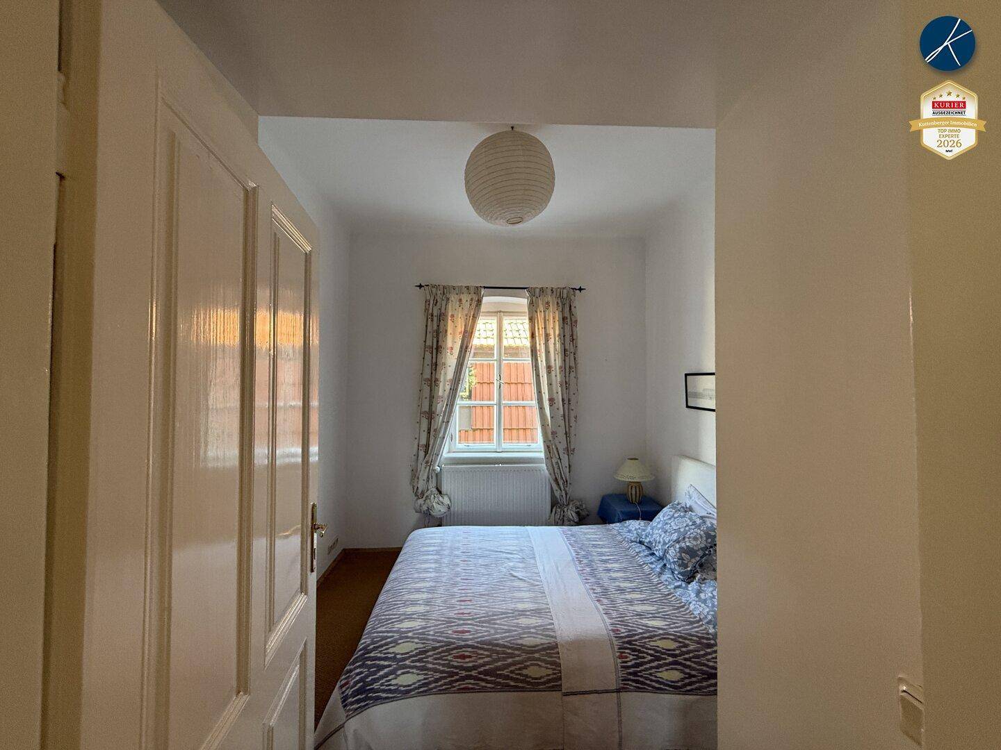 Helles Schlafzimmer mit weiß gestrichenen Wänden und einem Fenster, das natürliches Licht hereinlässt.