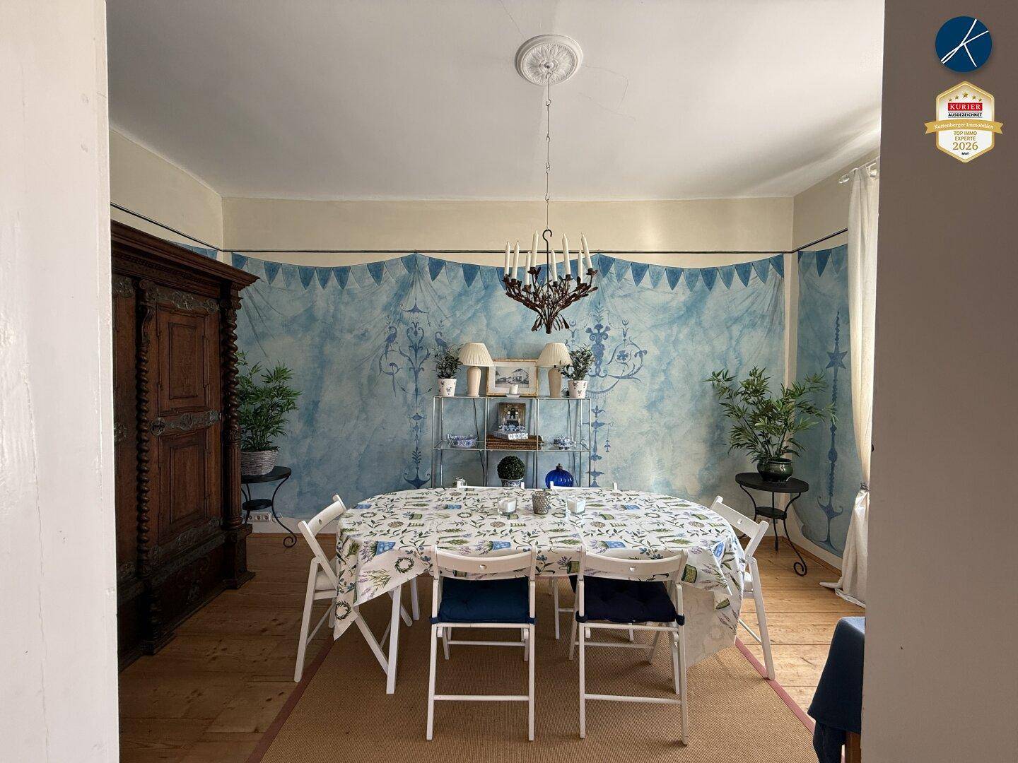Esszimmer mit Holzboden, blauer Wandgestaltung und einem großen Esstisch mit Stühlen.