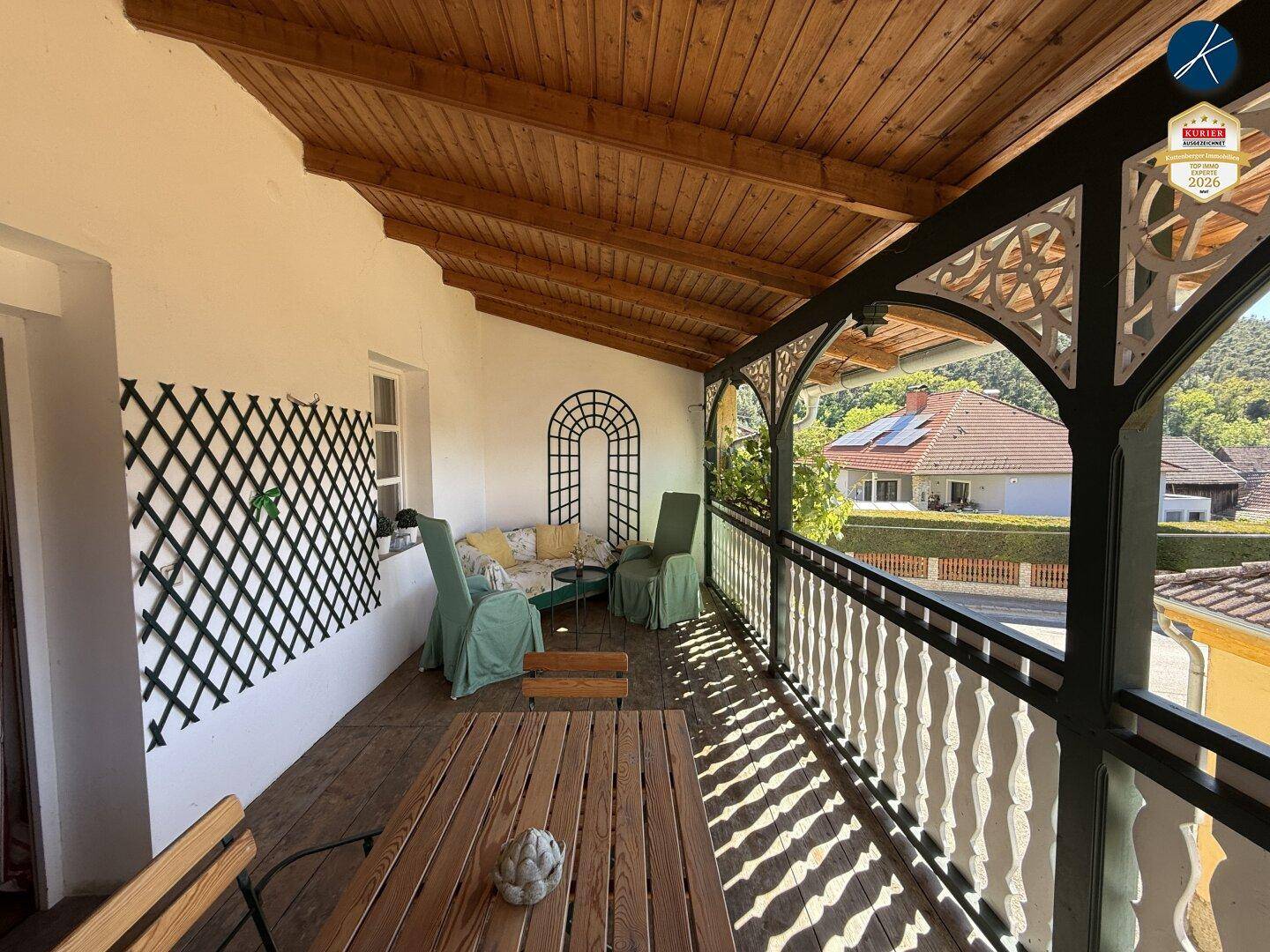 Überdachter Balkon mit Holzboden und Sitzgelegenheiten, bietet einen Blick auf die Umgebung.