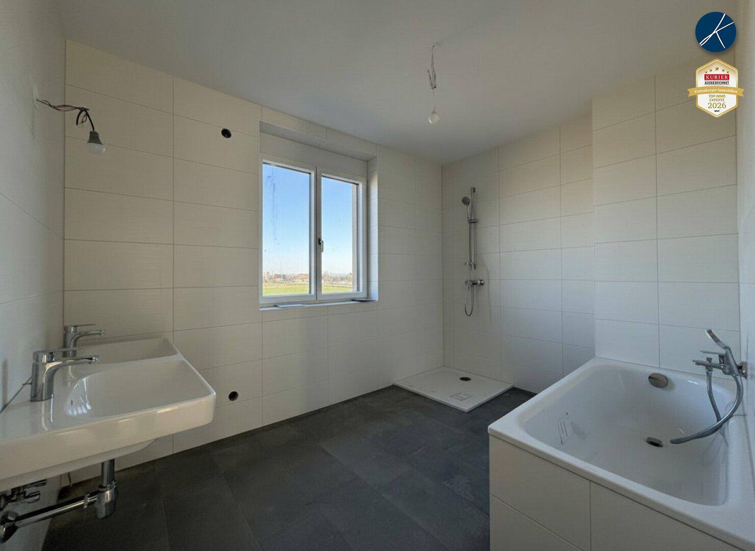Unmöbliertes Badezimmer mit Doppelwaschbecken, Dusche, Badewanne und Fenster.