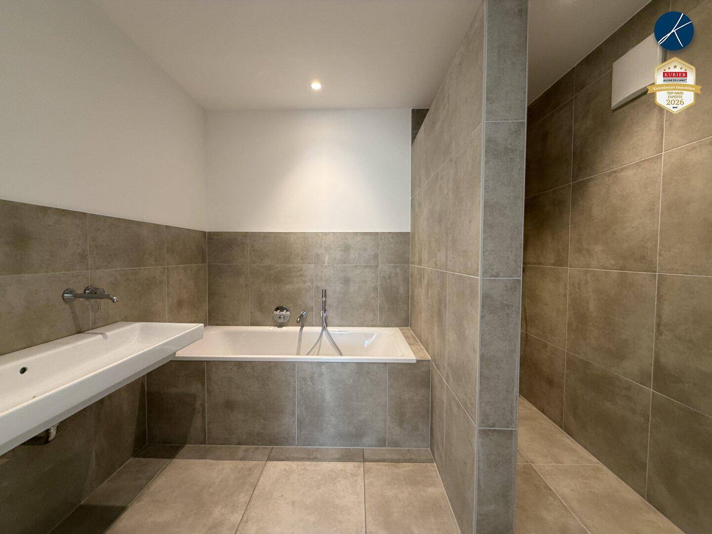 Modernes Badezimmer mit Badewanne, grauen Fliesen und schlichtem Waschbecken.