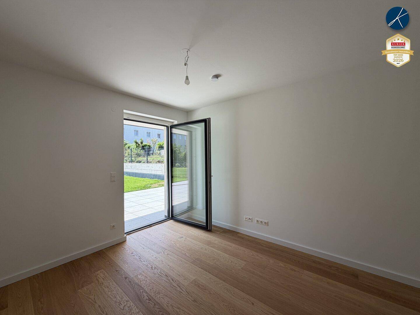 Leeres Schlafzimmer mit Holzboden und einer Tür, die zu einer Terrasse und dem Garten führt.