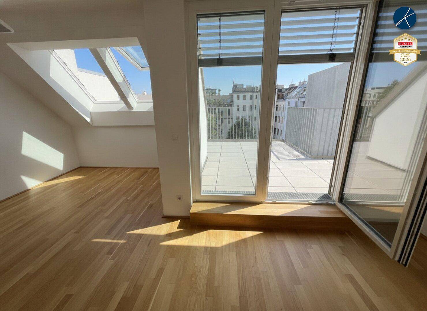 Heller Raum mit Holzboden, großen Fenstern und Zugang zu einer sonnigen Dachterrasse.