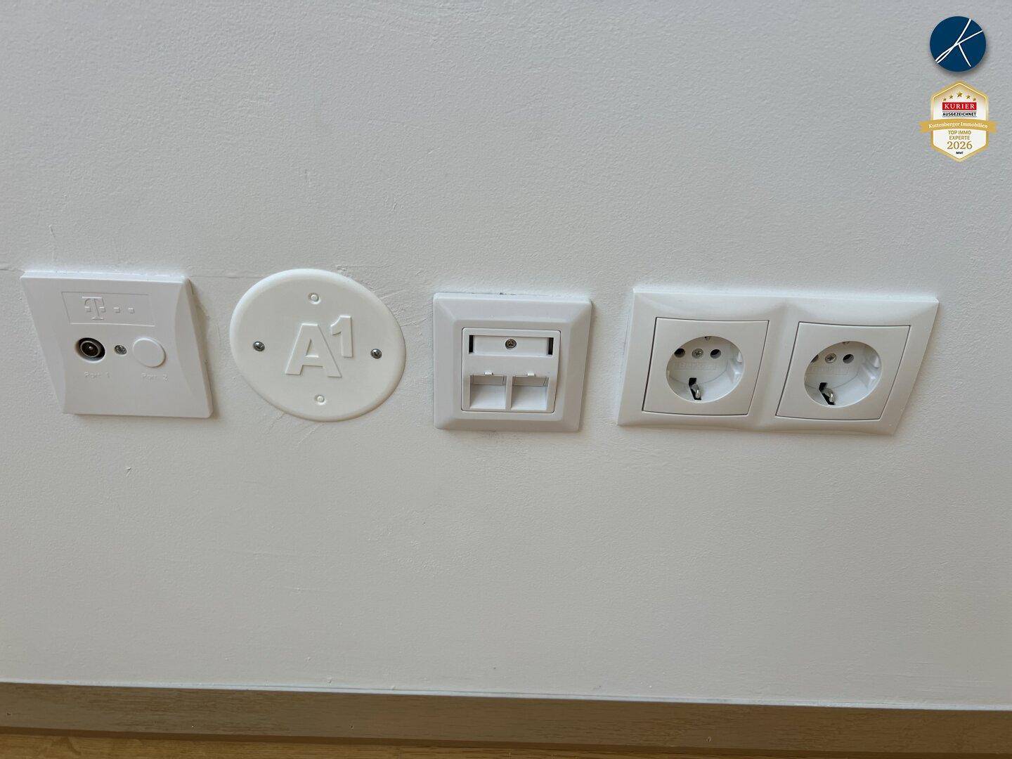 Wand mit verschiedenen Anschlüssen für TV, Internet und Stromversorgung.