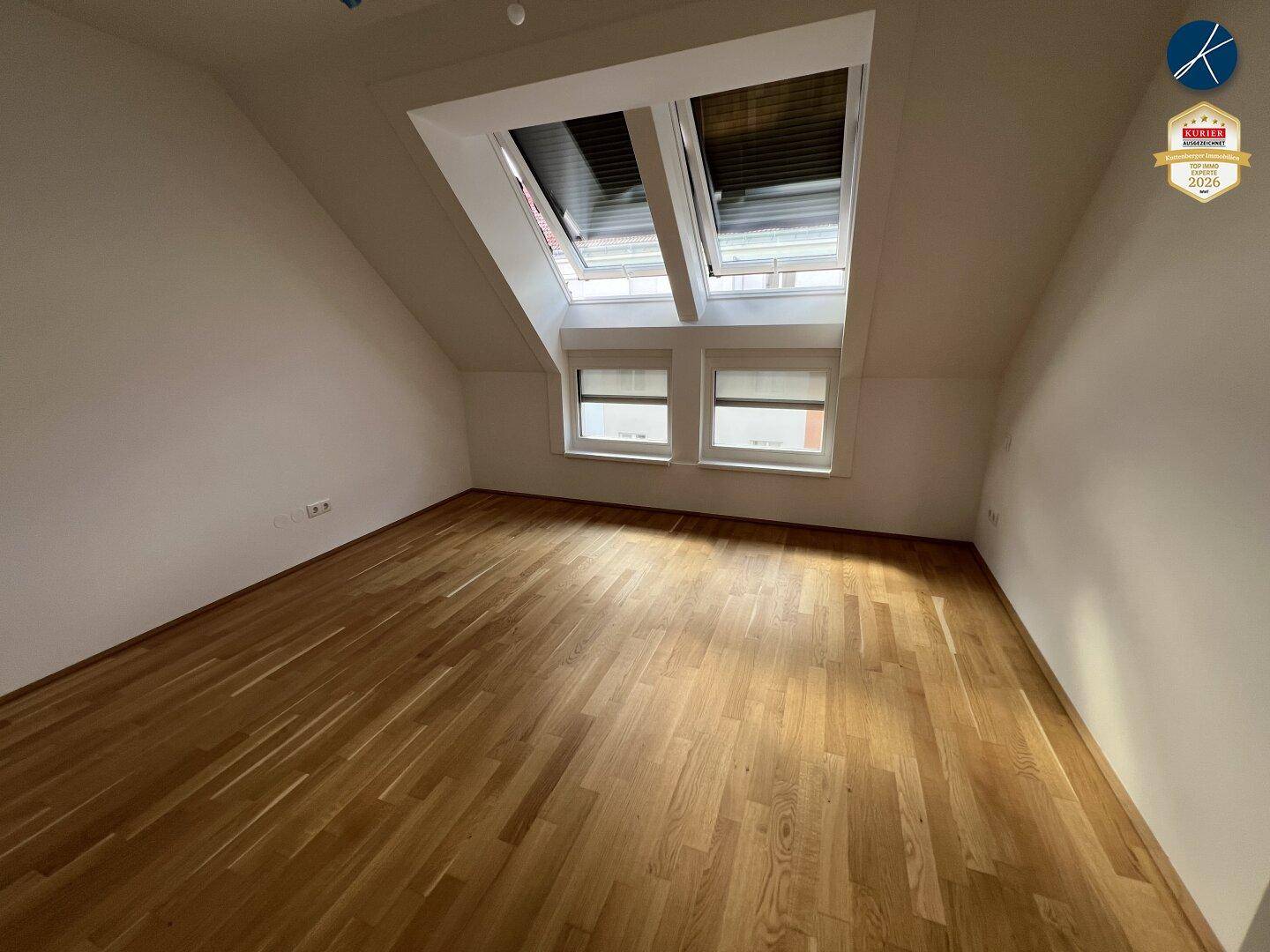 Helles Schlafzimmer mit Holzboden, Dachschrägen und mehreren Dachfenstern.