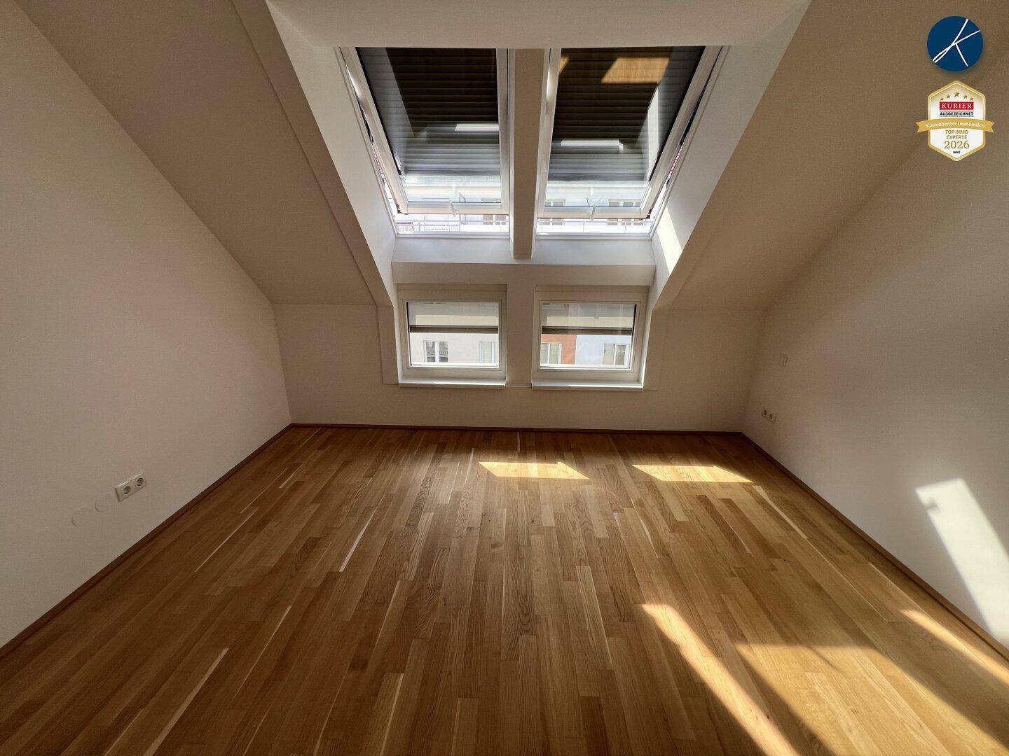 Geräumiges Schlafzimmer im Dachgeschoss mit Holzboden und viel Tageslicht durch Dachfenster.