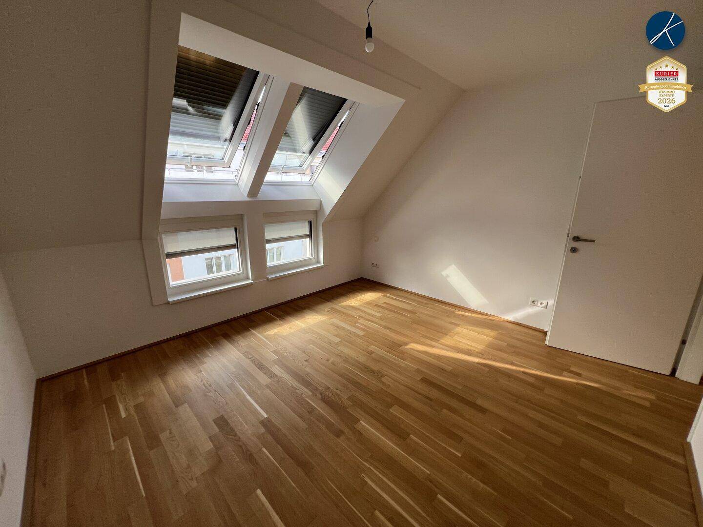 Lichtdurchflutetes Schlafzimmer mit Holzboden, Dachschrägen und Zugangstür.