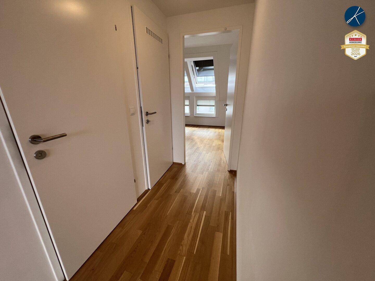 Heller Flur mit Holzboden und weißen Türen, der zu weiteren Räumen mit Dachfenstern führt.