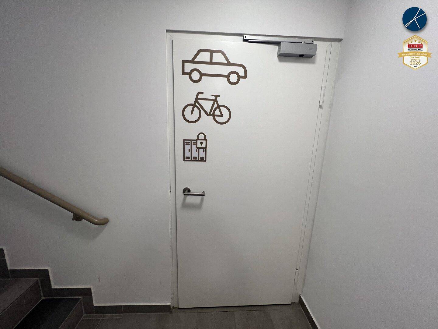 Weiße Tür mit Symbolen für Auto, Fahrrad und Gepäck, neben einer Treppe.