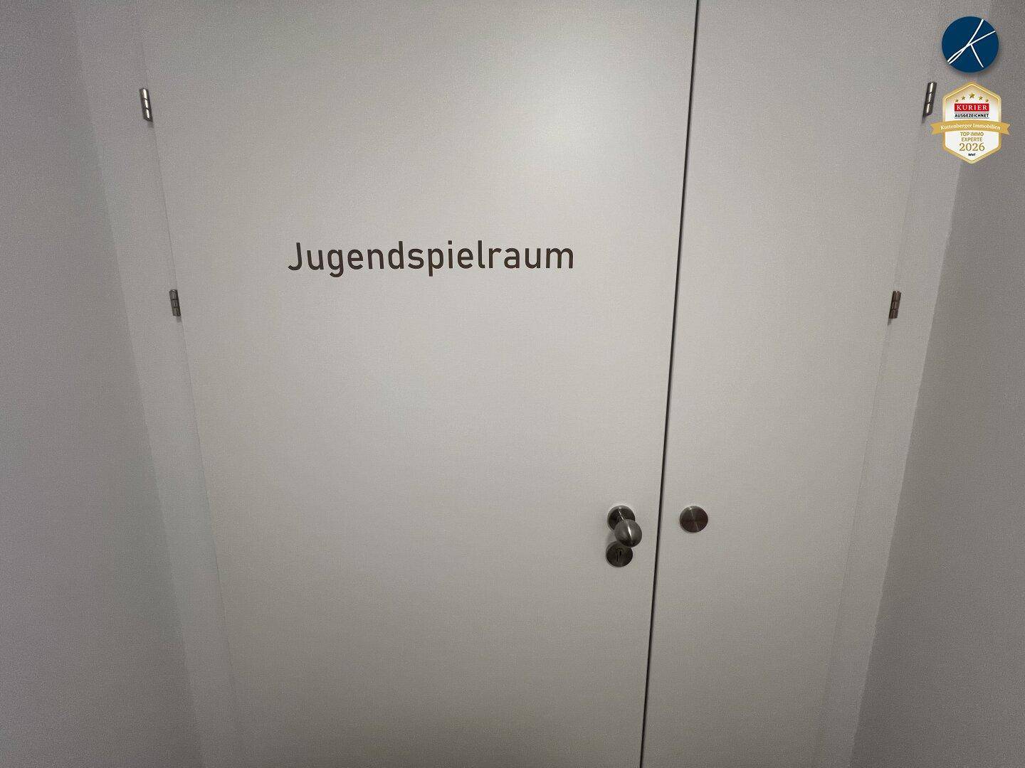 Weiße Tür mit der Aufschrift "Jugendspielraum", die zu einem Gemeinschaftsraum führt.