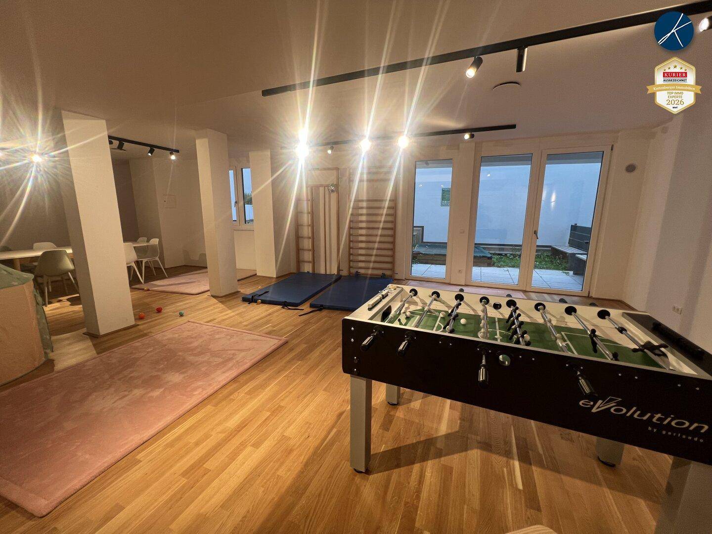 Heller Gemeinschaftsraum mit Tischfußball, Gymnastikmatten und Zugang zu einem Außenbereich.