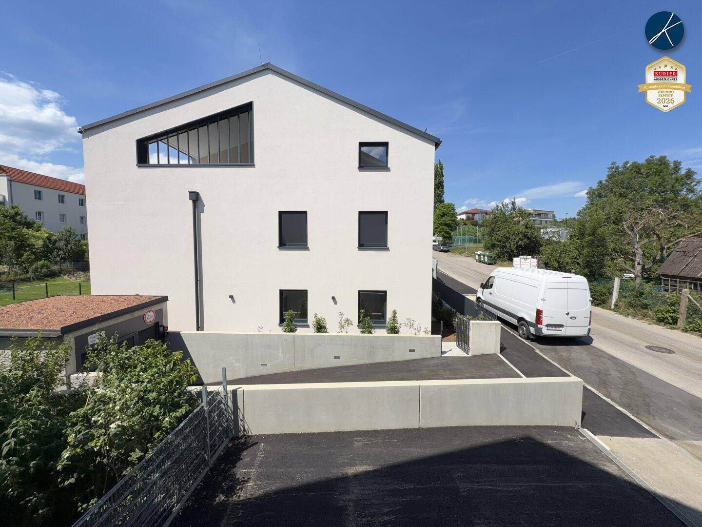 Seitenansicht des modernen Gebäudes mit markantem Fenster und Zufahrt.