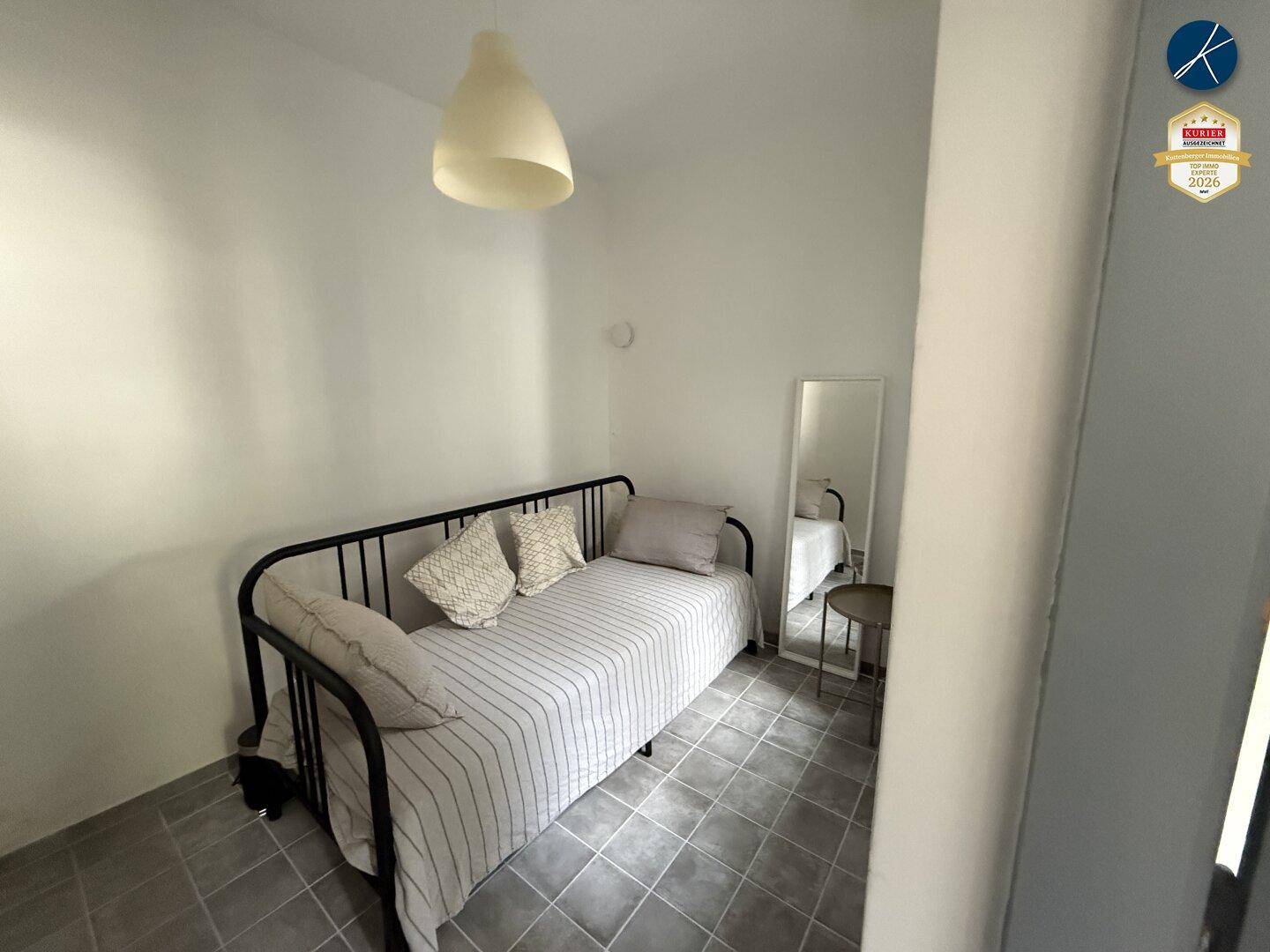 Kleines Schlafzimmer mit Einzelbett, Spiegel und Fliesenboden.
