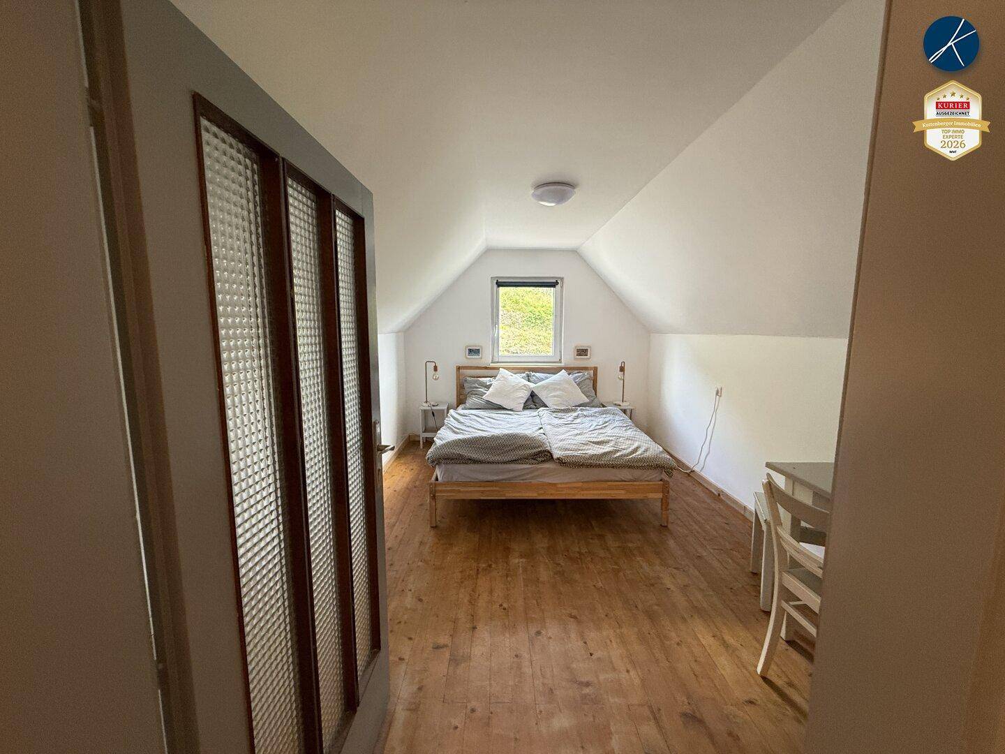 Helles Schlafzimmer im Dachgeschoss mit Holzboden und Blick ins Grüne.